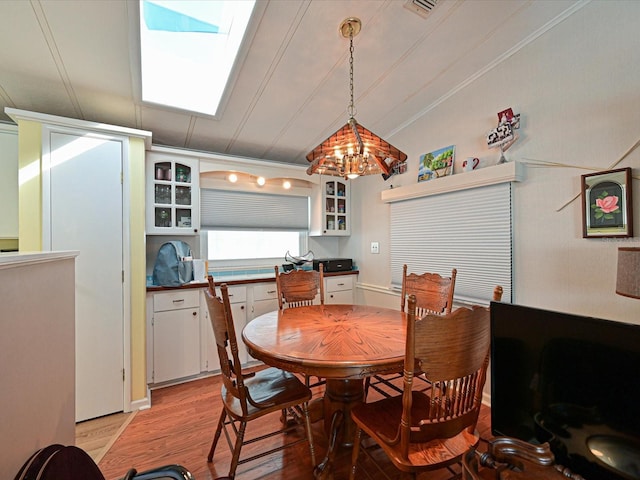 dining room with lofted ceiling with skylight, light wood-type flooring, and an inviting chandelier