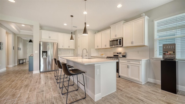 kitchen featuring stainless steel appliances, a kitchen island with sink, sink, white cabinetry, and hanging light fixtures