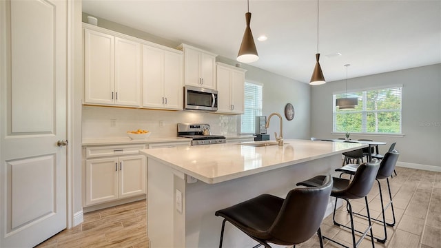 kitchen featuring stainless steel appliances, a kitchen island with sink, sink, pendant lighting, and white cabinetry