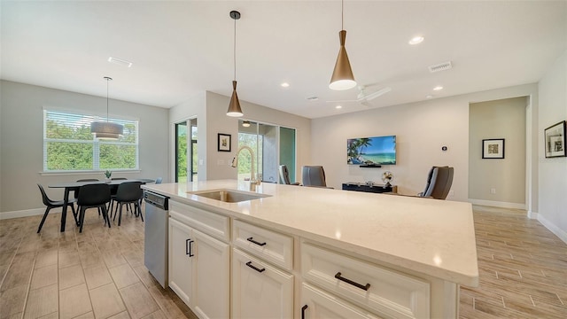 kitchen featuring dishwasher, sink, light stone counters, an island with sink, and decorative light fixtures