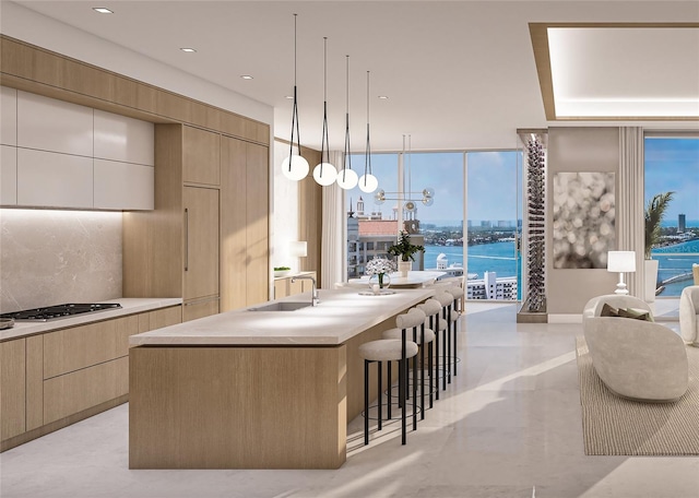 kitchen with backsplash, expansive windows, pendant lighting, a water view, and an island with sink