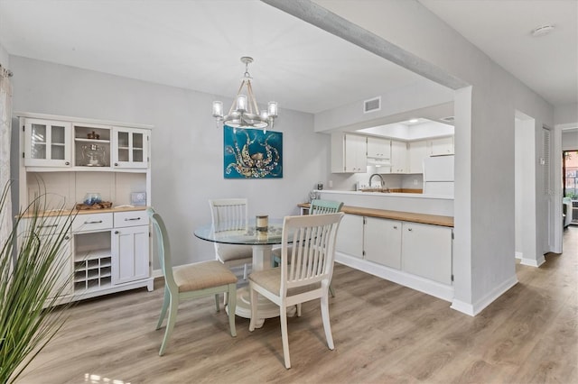 dining area with light hardwood / wood-style flooring, a notable chandelier, and sink