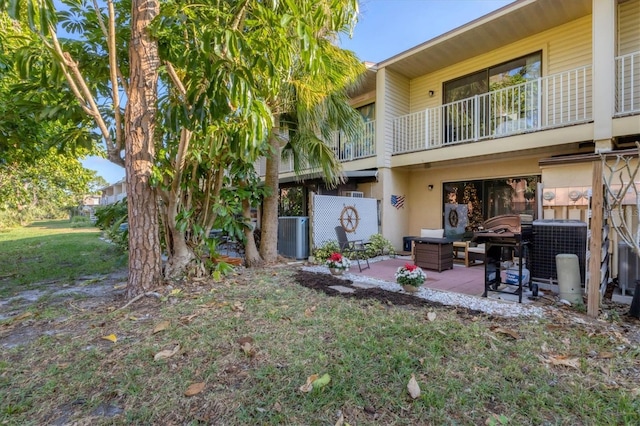 rear view of property featuring a yard, a balcony, central AC, and a patio area