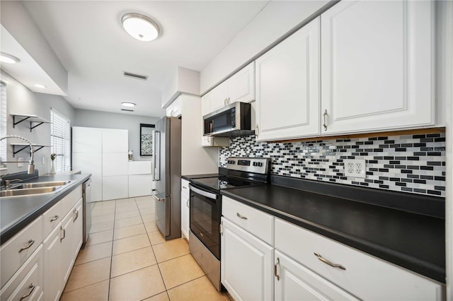 kitchen with appliances with stainless steel finishes, tasteful backsplash, sink, light tile patterned floors, and white cabinetry