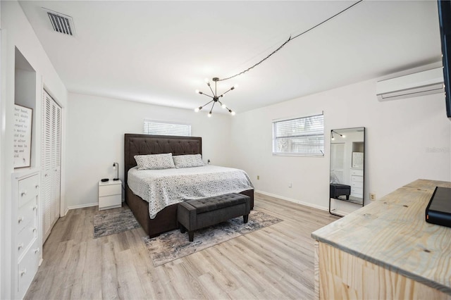 bedroom featuring a notable chandelier, light hardwood / wood-style floors, a wall unit AC, and a closet