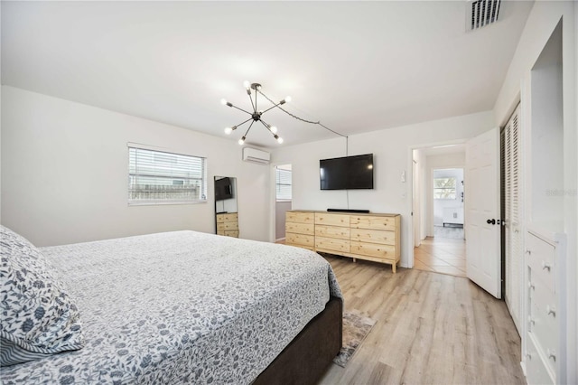 bedroom with a wall mounted air conditioner, light wood-type flooring, multiple windows, and a closet