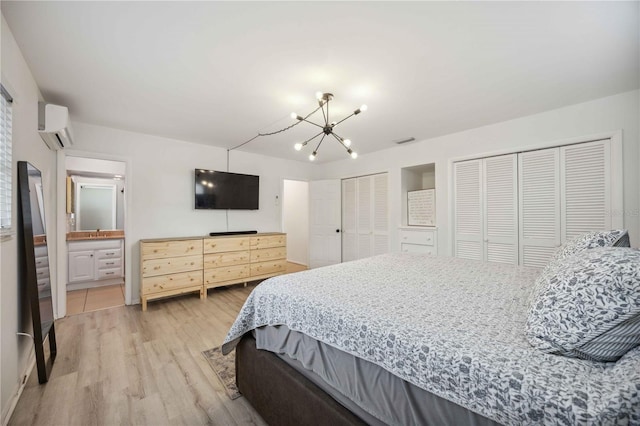 bedroom with multiple closets, ensuite bath, a wall mounted AC, hardwood / wood-style floors, and a chandelier