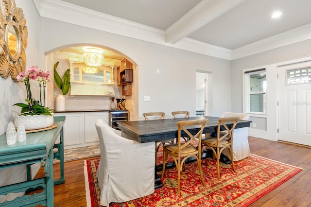 dining space with beam ceiling, beverage cooler, dark wood-type flooring, a notable chandelier, and crown molding