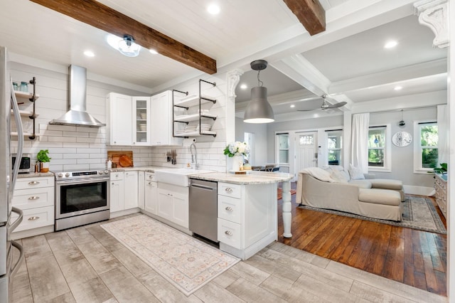 kitchen with white cabinets, wall chimney range hood, sink, appliances with stainless steel finishes, and beam ceiling