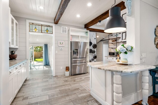 kitchen with stainless steel appliances, light stone counters, beamed ceiling, pendant lighting, and white cabinets