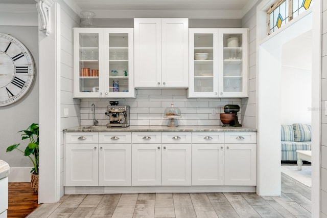 bar featuring white cabinetry, sink, tasteful backsplash, light stone counters, and ornamental molding