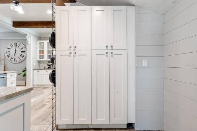 kitchen featuring decorative backsplash, light stone counters, beamed ceiling, white cabinets, and wood walls