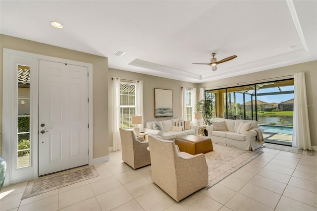 living room with a raised ceiling, a water view, ceiling fan, and light tile patterned floors