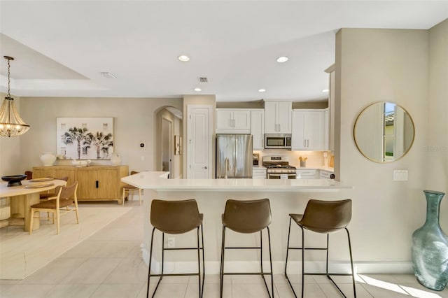 kitchen with a breakfast bar, light tile patterned floors, appliances with stainless steel finishes, decorative light fixtures, and white cabinetry