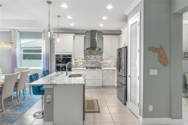 kitchen featuring a kitchen island with sink, wall chimney range hood, sink, appliances with stainless steel finishes, and white cabinetry