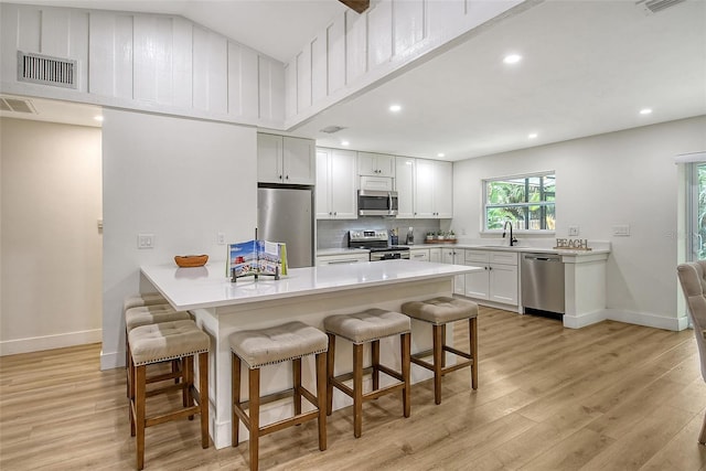 kitchen with light wood-type flooring, tasteful backsplash, stainless steel appliances, white cabinets, and a breakfast bar area