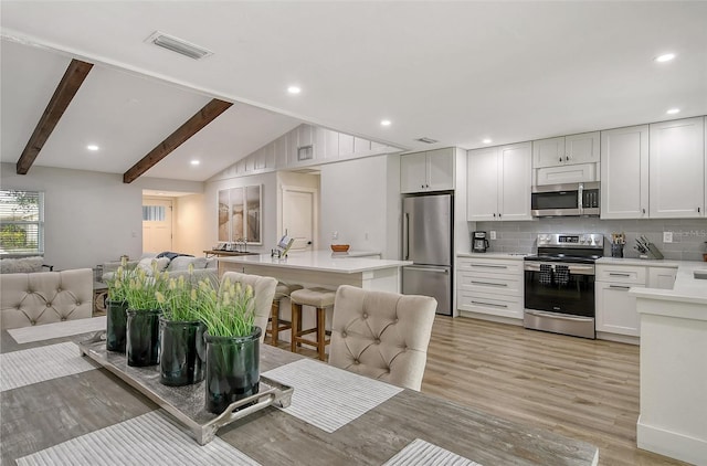 kitchen featuring tasteful backsplash, a kitchen island, a kitchen bar, white cabinetry, and stainless steel appliances