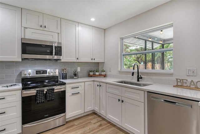 kitchen with sink, light hardwood / wood-style flooring, decorative backsplash, white cabinetry, and stainless steel appliances