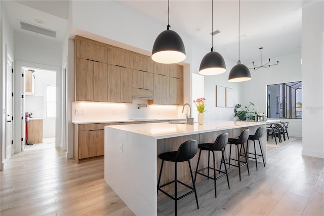 kitchen featuring light hardwood / wood-style flooring, light brown cabinets, hanging light fixtures, a large island with sink, and a kitchen breakfast bar