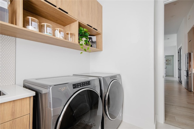 clothes washing area with cabinets, separate washer and dryer, and light hardwood / wood-style floors