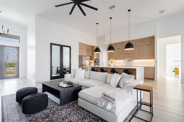 living room featuring light hardwood / wood-style flooring, french doors, ceiling fan, and a high ceiling