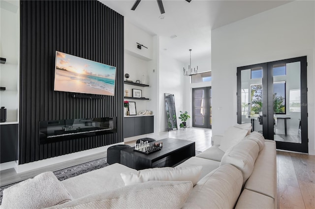 living room featuring french doors, an inviting chandelier, built in features, light hardwood / wood-style floors, and a high ceiling