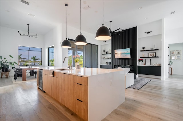 kitchen with pendant lighting, a spacious island, sink, beverage cooler, and light hardwood / wood-style flooring