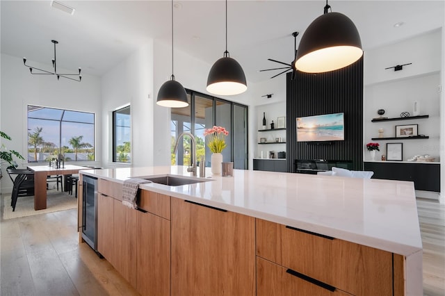 kitchen with sink, beverage cooler, hanging light fixtures, light wood-type flooring, and a spacious island