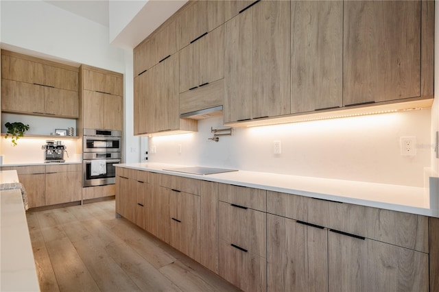 kitchen featuring extractor fan, double oven, black electric stovetop, light brown cabinets, and light wood-type flooring