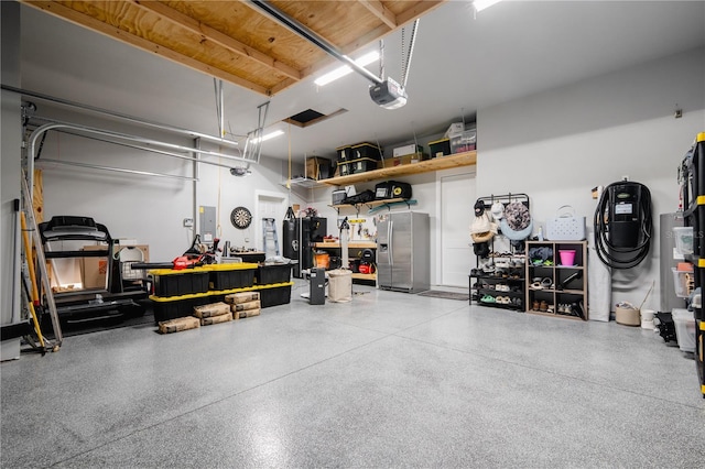 garage featuring electric panel, stainless steel fridge with ice dispenser, a garage door opener, black fridge, and a workshop area