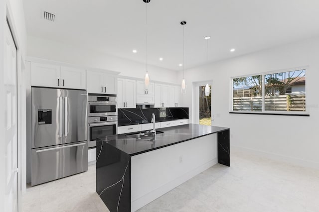 kitchen featuring white cabinets, hanging light fixtures, sink, an island with sink, and appliances with stainless steel finishes