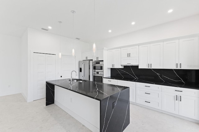 kitchen featuring stainless steel appliances, an island with sink, pendant lighting, decorative backsplash, and white cabinets