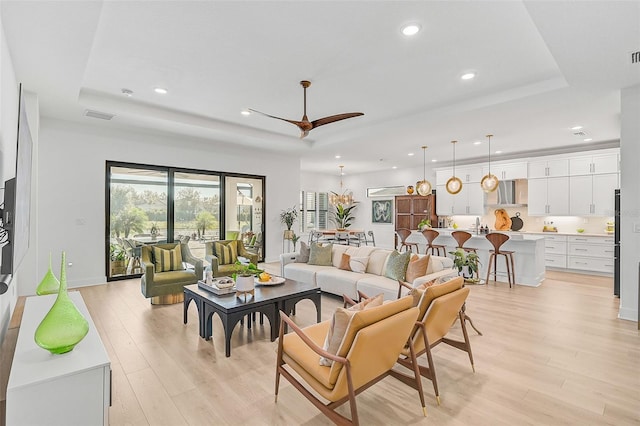 living room featuring a tray ceiling, ceiling fan, and light wood-type flooring