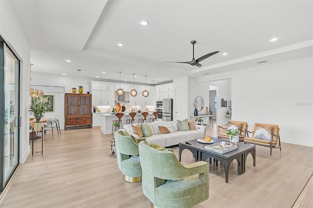 living room with ceiling fan with notable chandelier and light hardwood / wood-style flooring