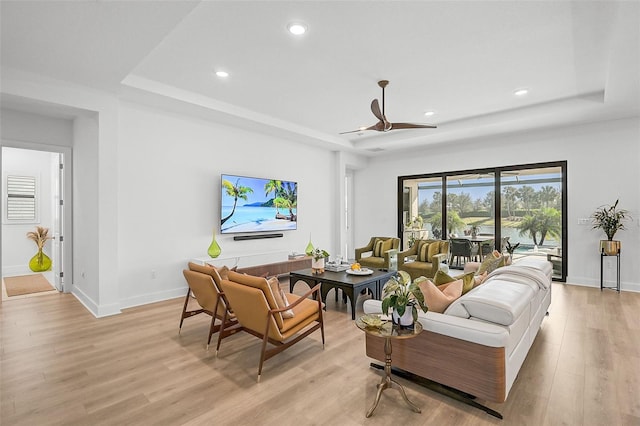 living room featuring a raised ceiling, ceiling fan, and light hardwood / wood-style flooring