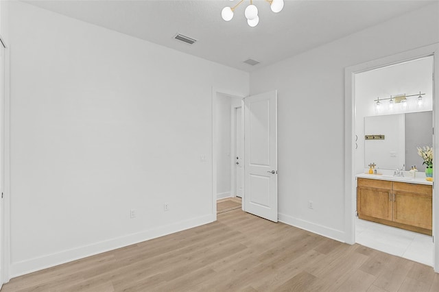 unfurnished bedroom featuring connected bathroom, sink, a notable chandelier, and light hardwood / wood-style flooring