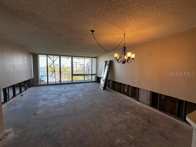 unfurnished room featuring a notable chandelier, expansive windows, concrete flooring, and a textured ceiling