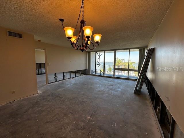 unfurnished living room with a chandelier, a textured ceiling, and a wall of windows