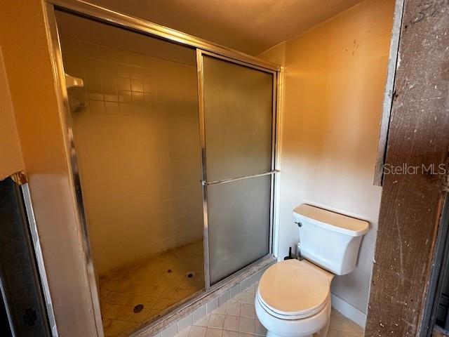 bathroom with tile patterned flooring, a shower with shower door, and toilet