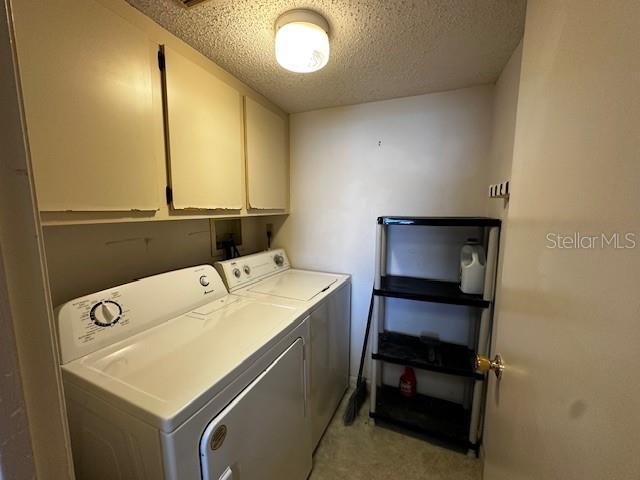 laundry room with cabinets, a textured ceiling, and separate washer and dryer