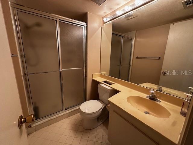 bathroom featuring tile patterned flooring, vanity, a shower with shower door, and toilet