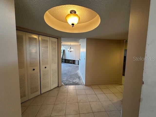 hallway featuring light tile patterned floors, a raised ceiling, and a notable chandelier