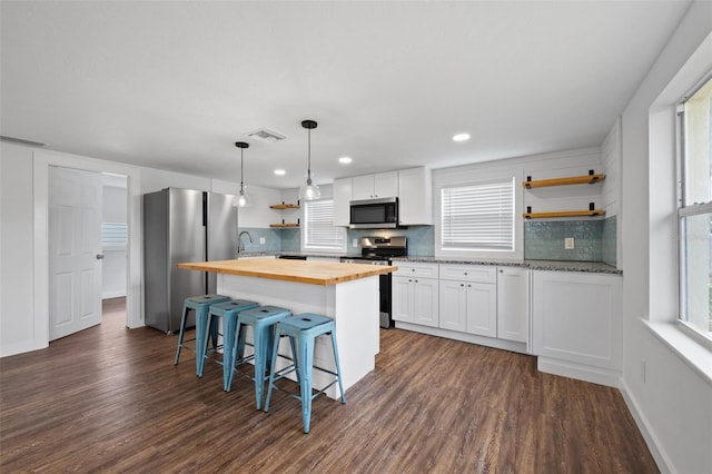 kitchen with appliances with stainless steel finishes, dark wood-type flooring, white cabinetry, a kitchen island, and butcher block counters