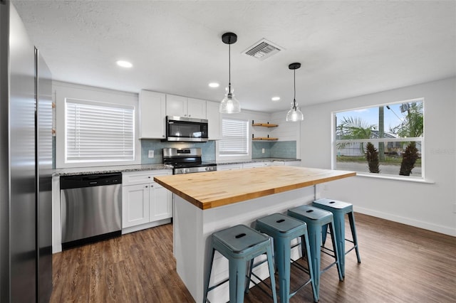 kitchen with a kitchen bar, wooden counters, white cabinets, and stainless steel appliances