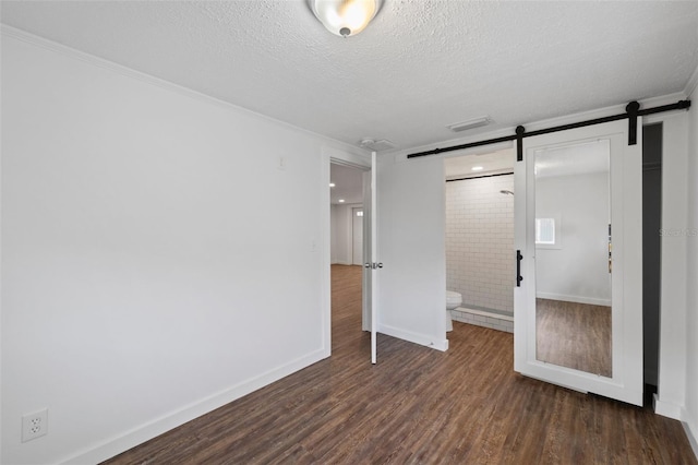 unfurnished bedroom featuring a barn door, a textured ceiling, connected bathroom, and dark wood-type flooring