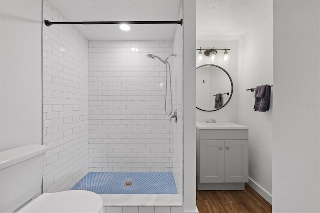 bathroom with hardwood / wood-style flooring, toilet, vanity, and tiled shower