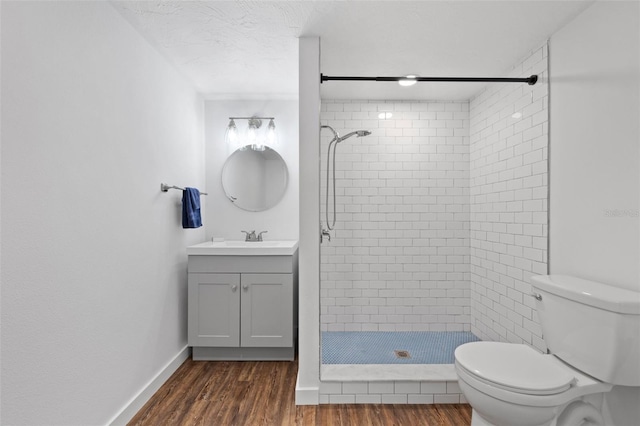 bathroom with a tile shower, vanity, a textured ceiling, hardwood / wood-style floors, and toilet