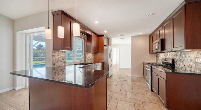 kitchen featuring kitchen peninsula, appliances with stainless steel finishes, sink, decorative light fixtures, and dark stone countertops