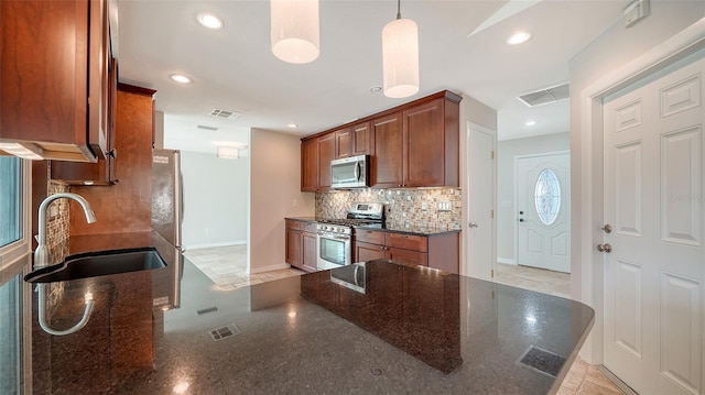 kitchen featuring appliances with stainless steel finishes, decorative light fixtures, dark stone countertops, and sink