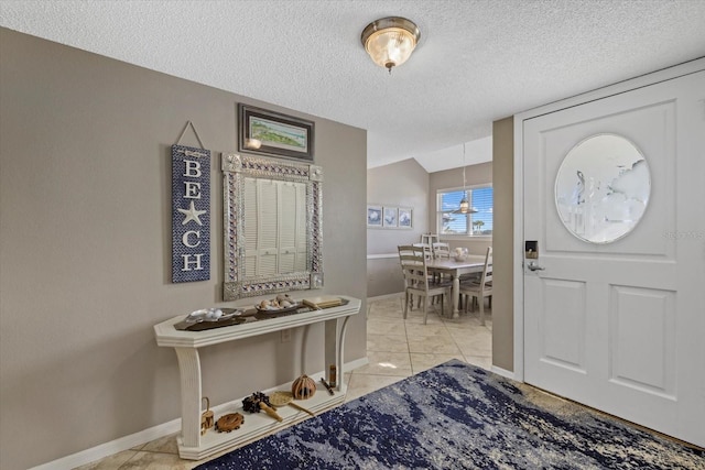 foyer entrance featuring a textured ceiling, vaulted ceiling, and light tile patterned floors